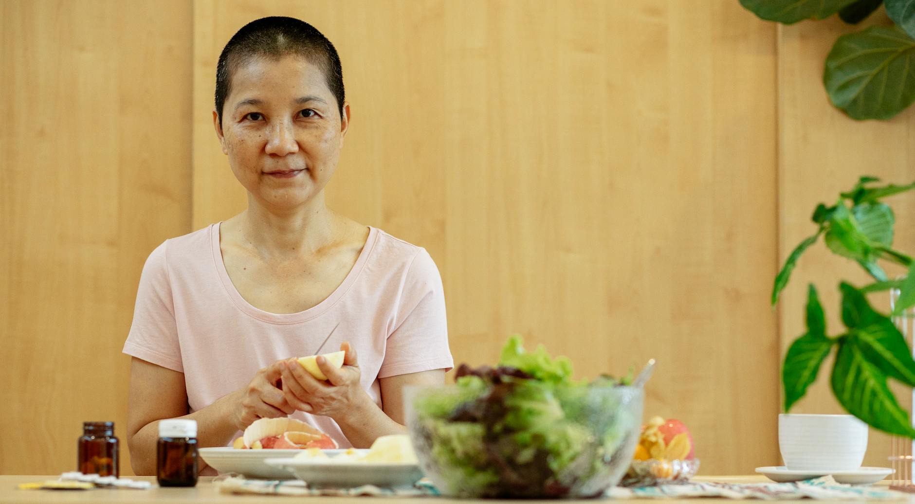 Cheerful ethnic ill female with short hair suffering from cancer at table with jars of medicines in daytime